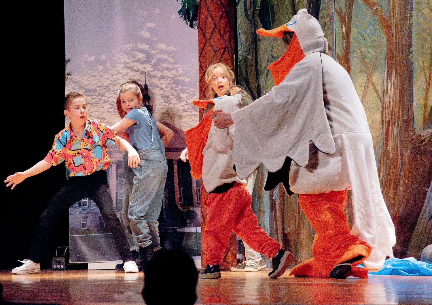 Dancers in colorful costumes perform dynamic movements on a theatrical stage.