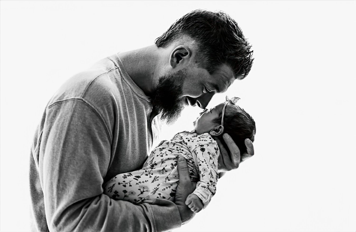 A tender black and white photograph showing a parent cradling and looking lovingly at their newborn baby.