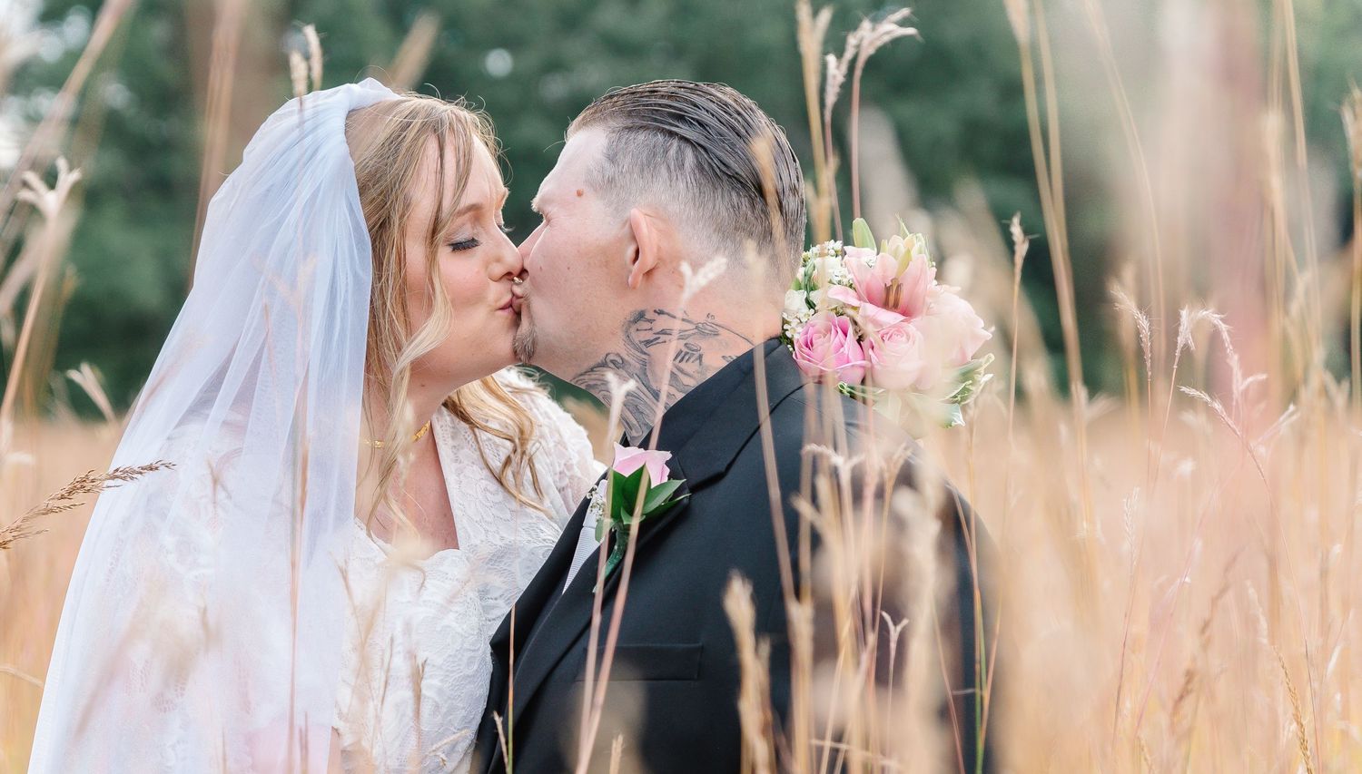 Romantic moment captured in golden wheat field with bridal veil flowing.