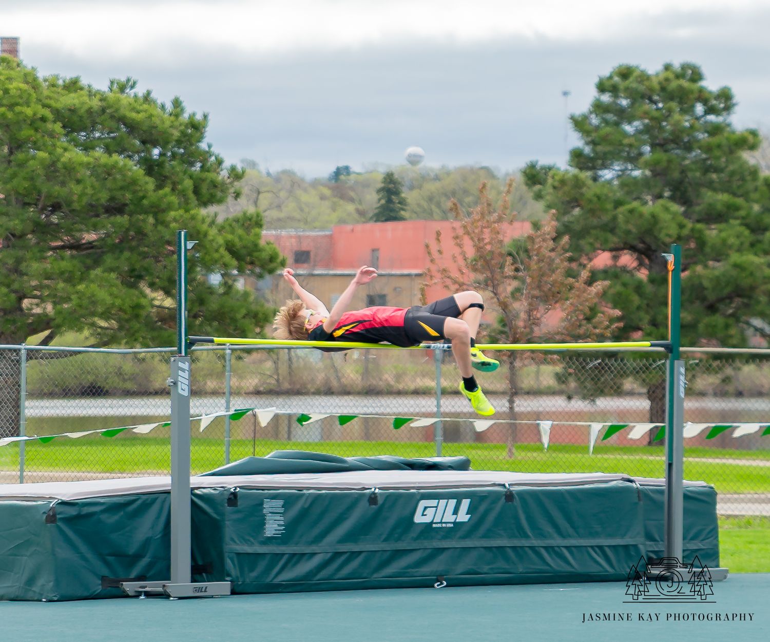 Track athlete executing Fosbury Flop technique over high jump bar with landing mat below.
