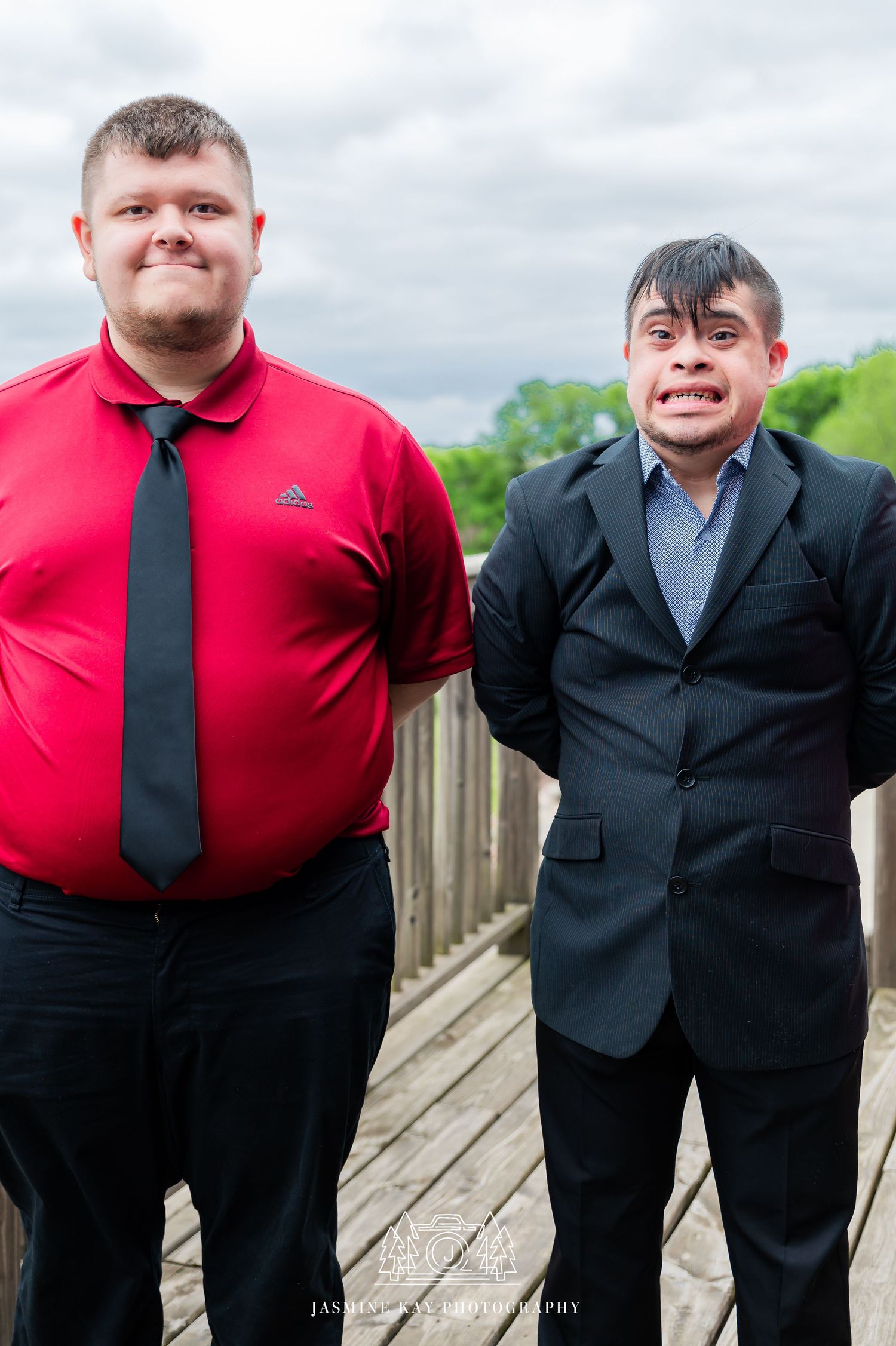 Two people in formal attire stand together on a wooden deck wearing red shirts and black ties.