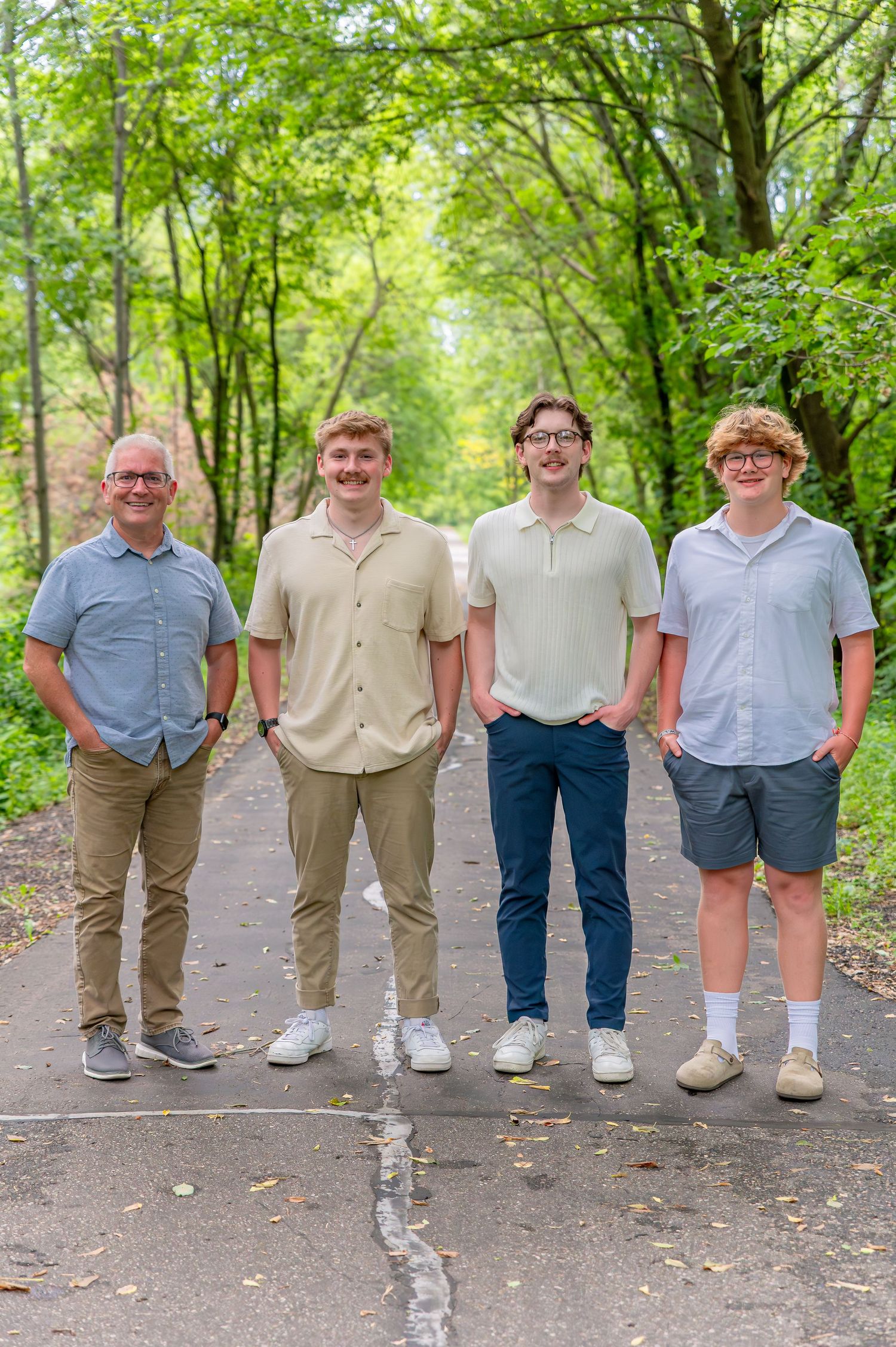 A group of friends stand together on a wooded path wearing coordinated casual outfits in earth tones and light colors.