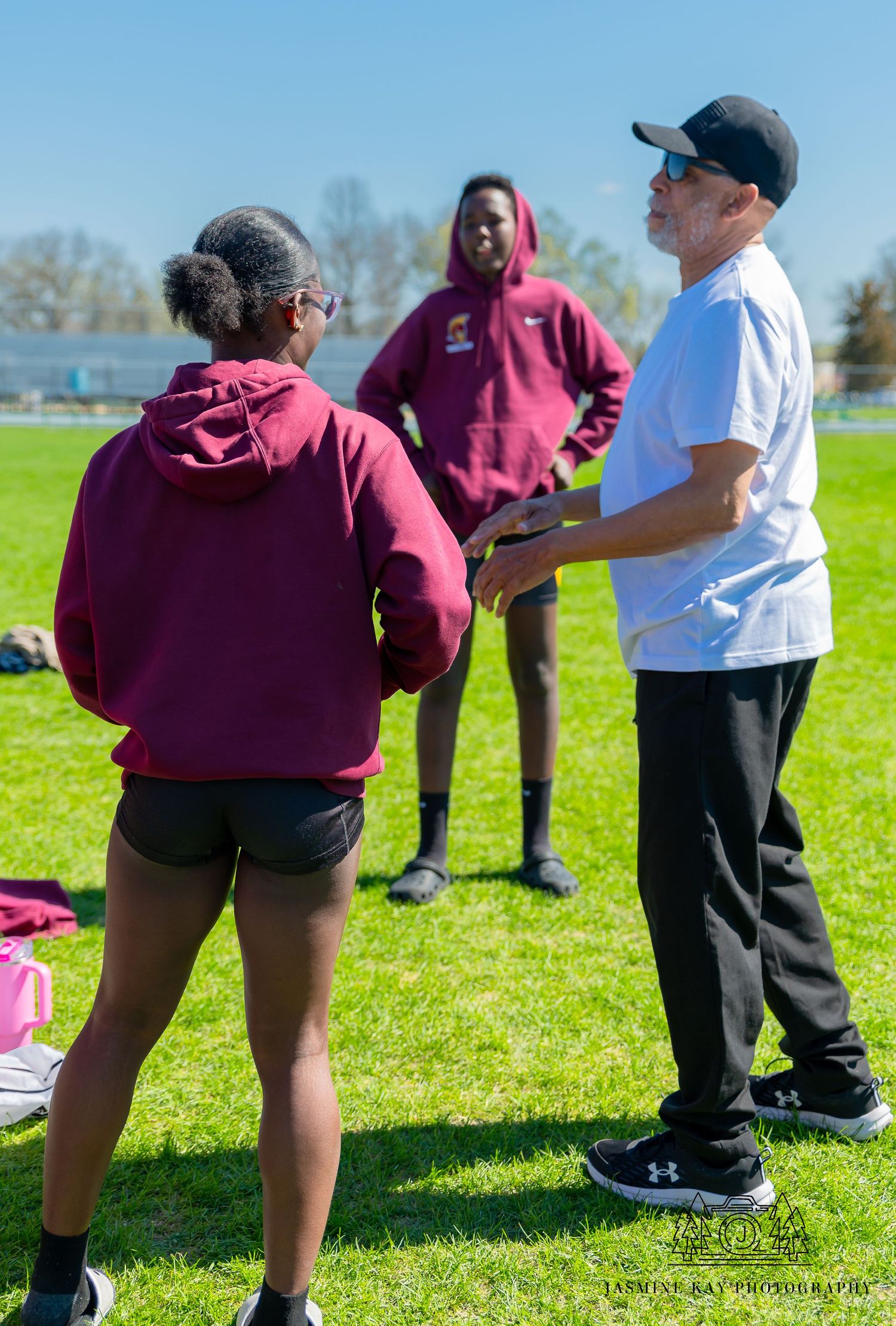 Athletes and coach having a discussion on a sunny day at a sports field.