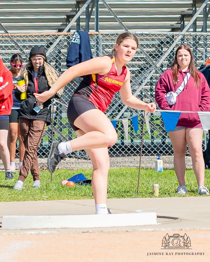 Athletes perform stretching exercises on bleachers during an outdoor track and field event.