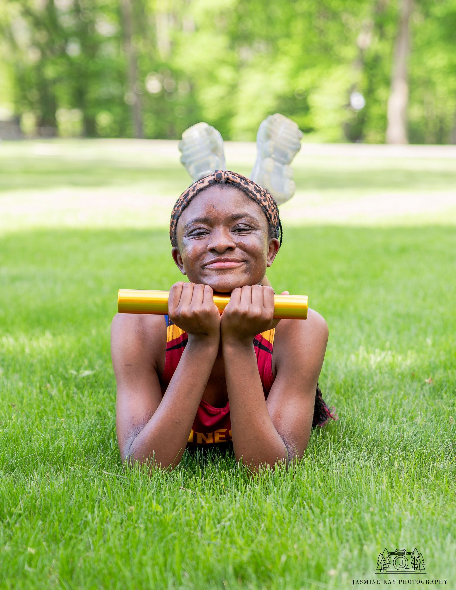 A person in red athletic wear lying on grass while holding yellow exercise equipment and smiling.