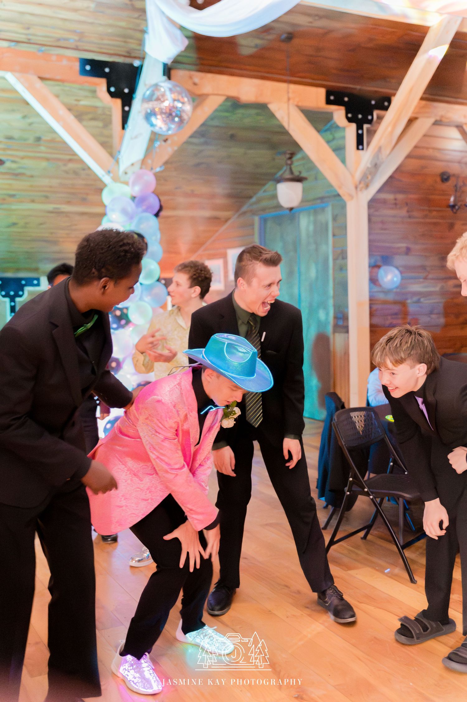 Group of dancers practicing dance moves together in a rustic wooden studio space with string lights overhead.