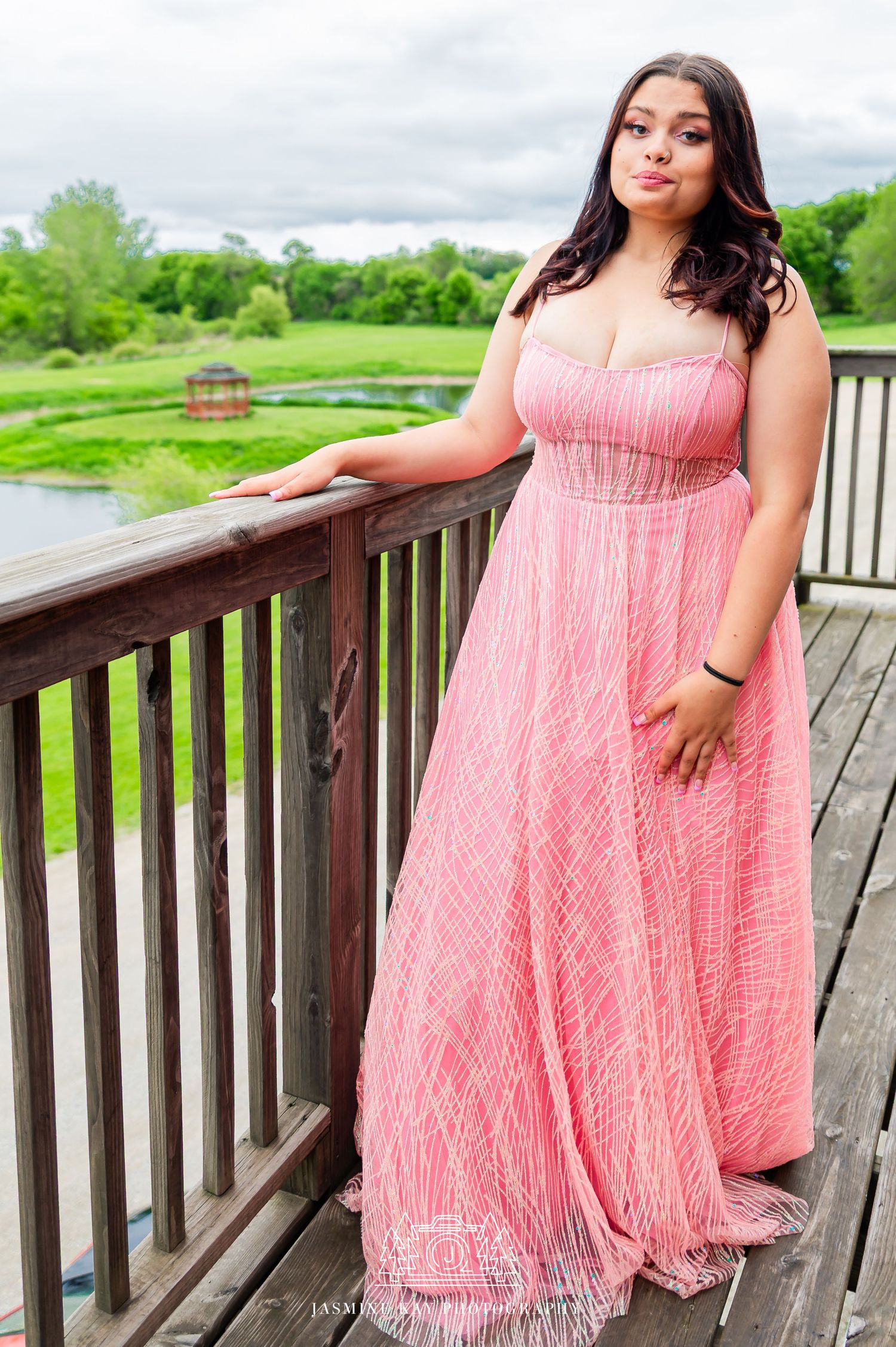 A pink flowy maxi dress with empire waist design photographed on a wooden deck overlooking a green landscape.