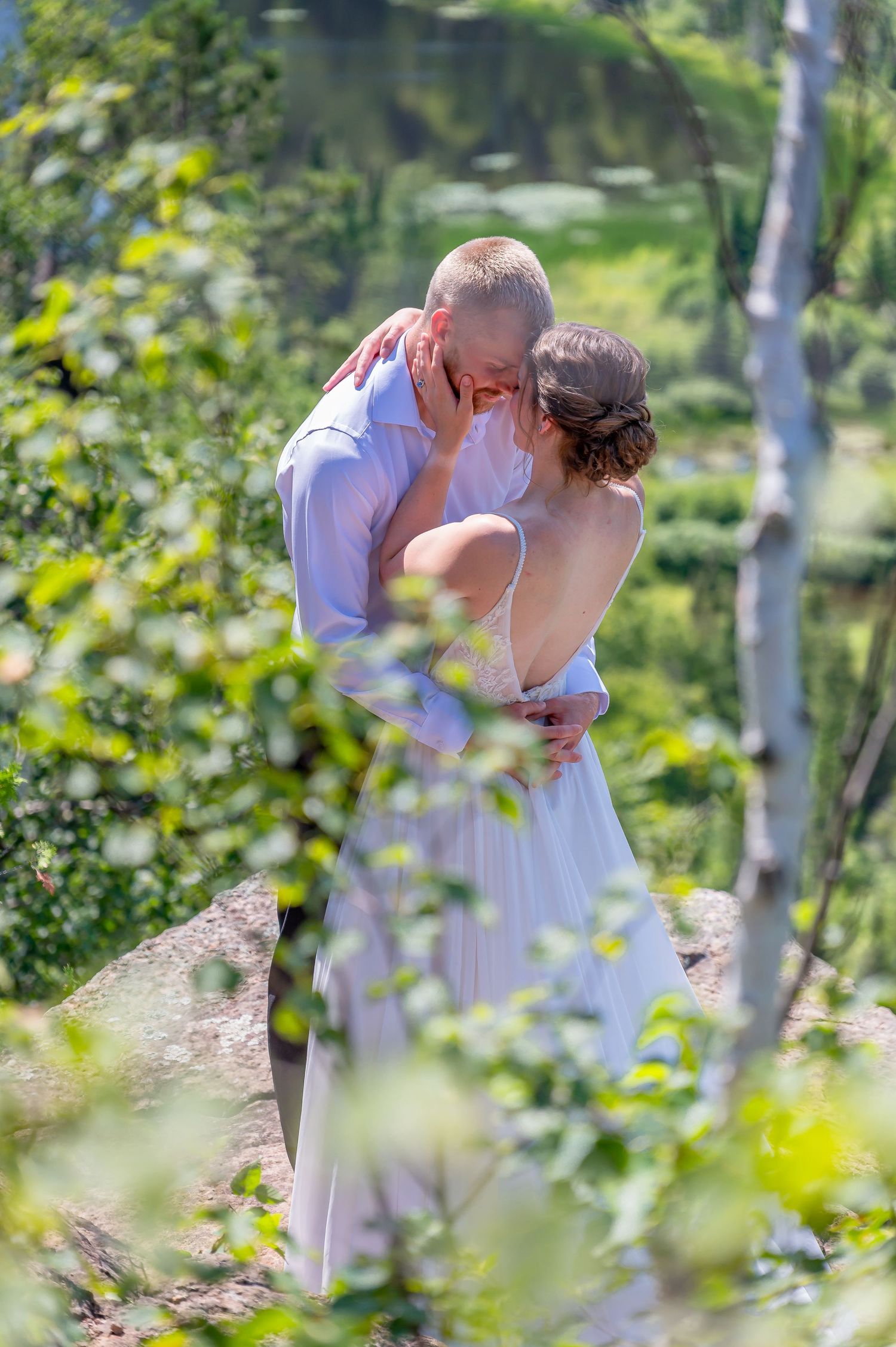 Couple shares tender moment among birch trees and greenery in summer forest setting.