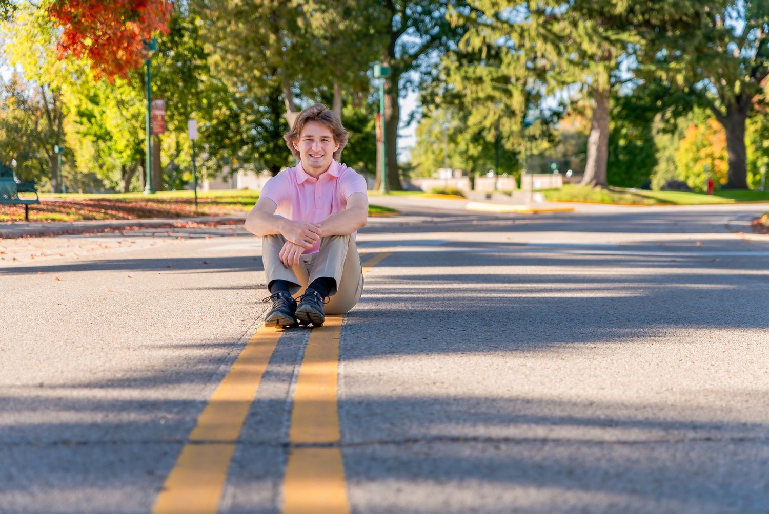 A person rides a skateboard down a sunny suburban street while casting a long shadow on the pavement.