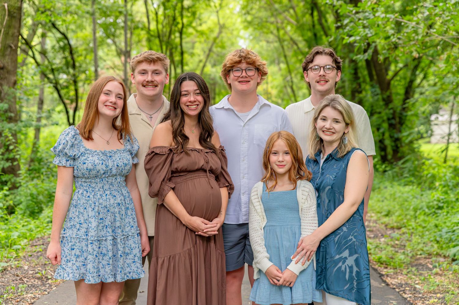 A group of people in coordinated blue and brown outfits pose together outdoors in a lush green forest setting.
