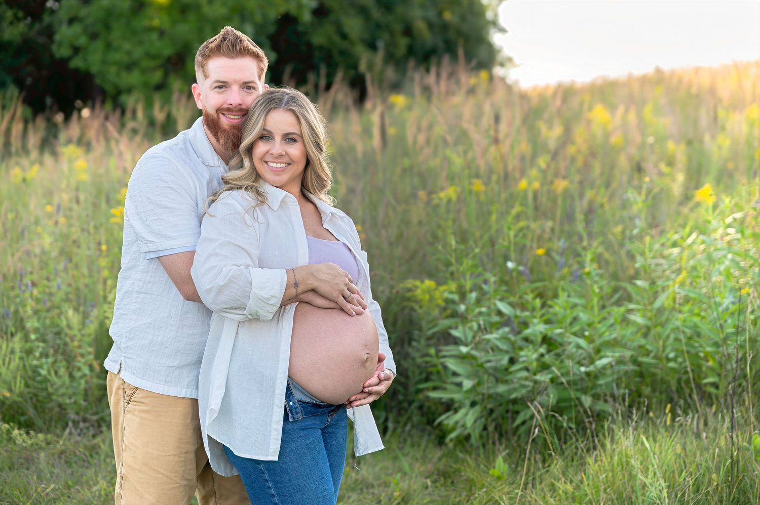 A couple embraces in a golden field of wildflowers during sunset for their engagement photos.