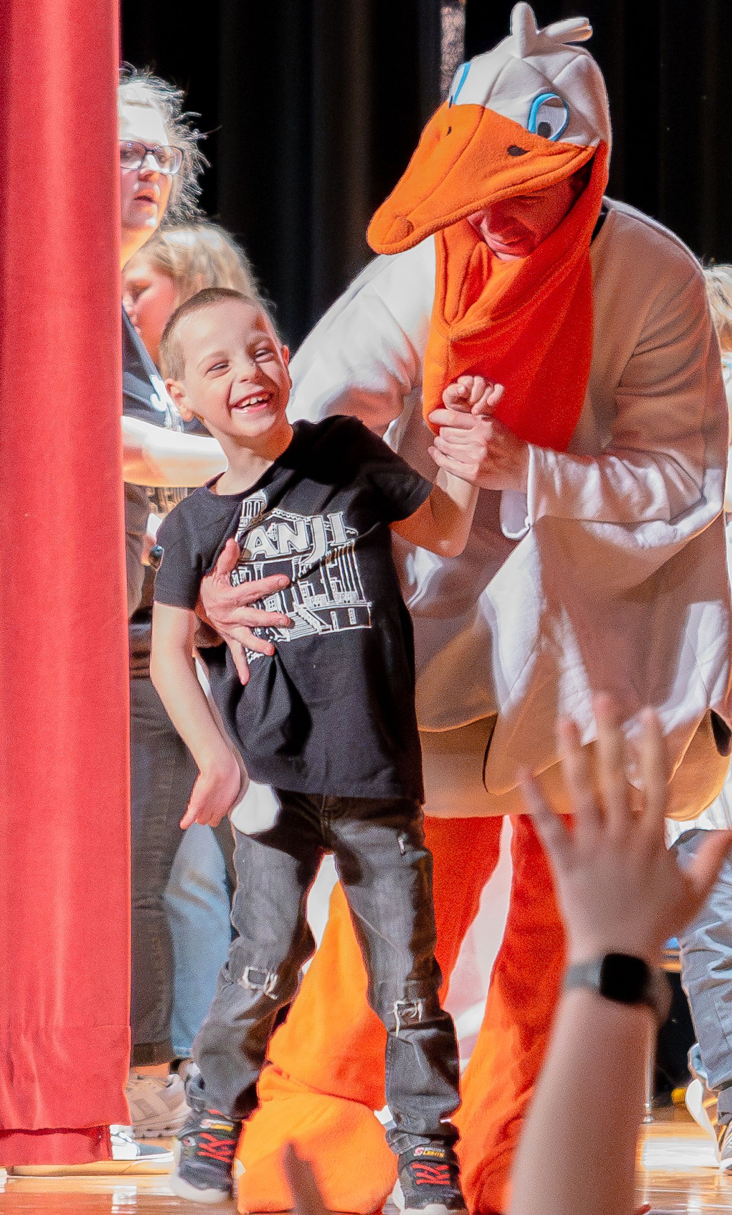 Performance sequence showing interaction between a person and an orange costumed character on a red-pillared stage.
