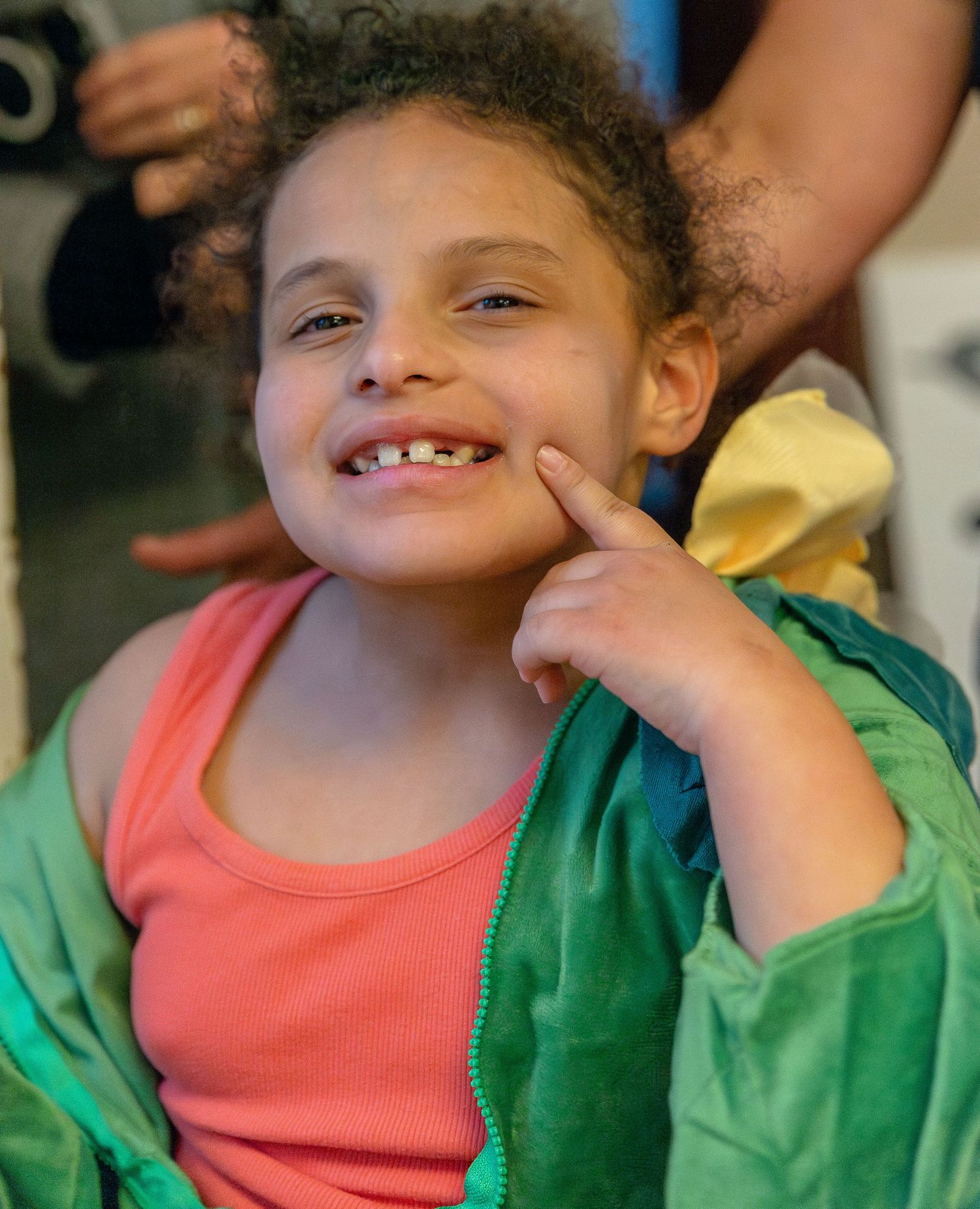 A child wearing a green jacket and coral shirt smiling in a sequence of candid shots.