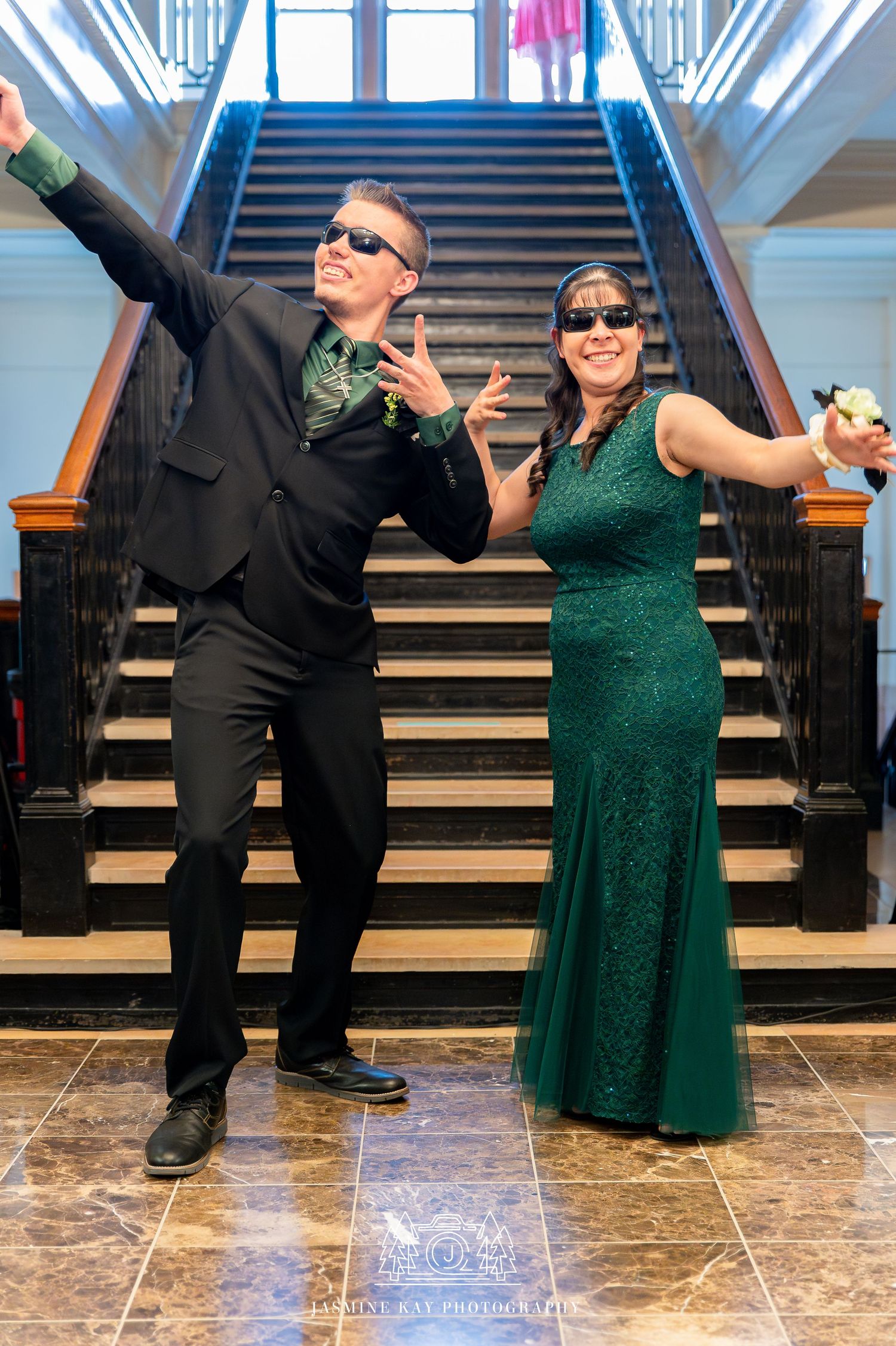 Two people in formal attire strike playful dance poses on a grand staircase in a series of four photos.