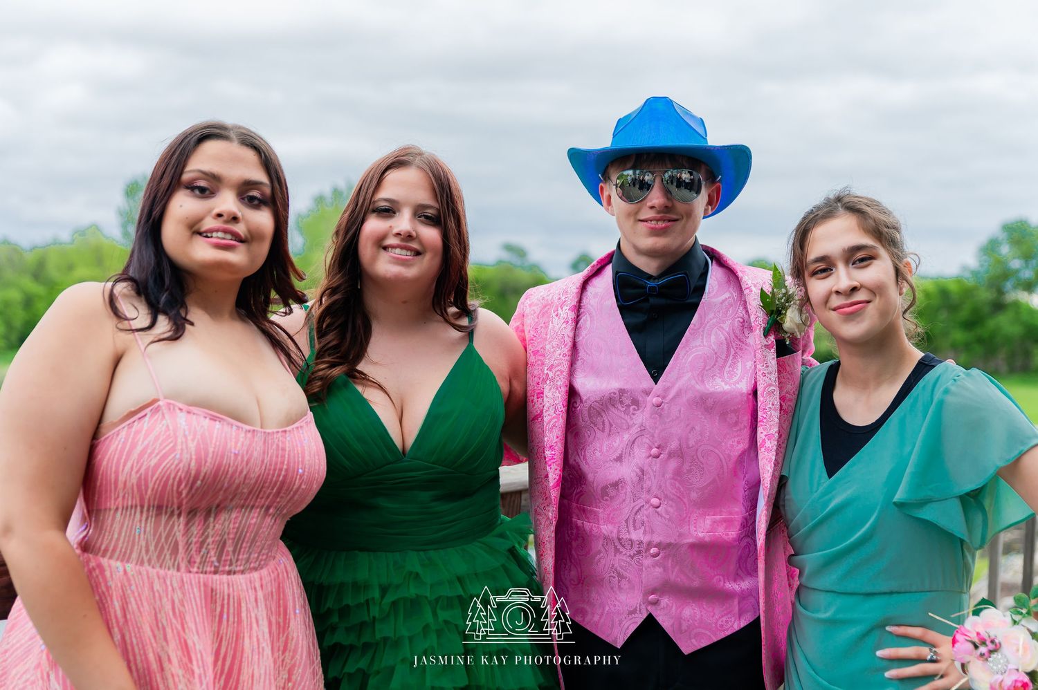 Wedding party members in coordinating pink, green, and purple outfits pose together outdoors.