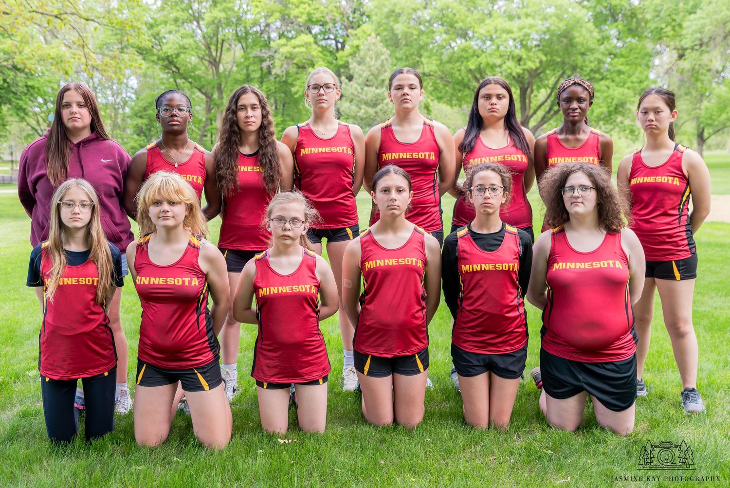 A group of athletes in red jerseys pose together on green grass for a team photo.