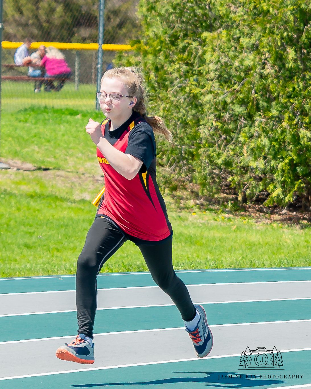 Athlete in red jersey and black pants running on outdoor track during competition.