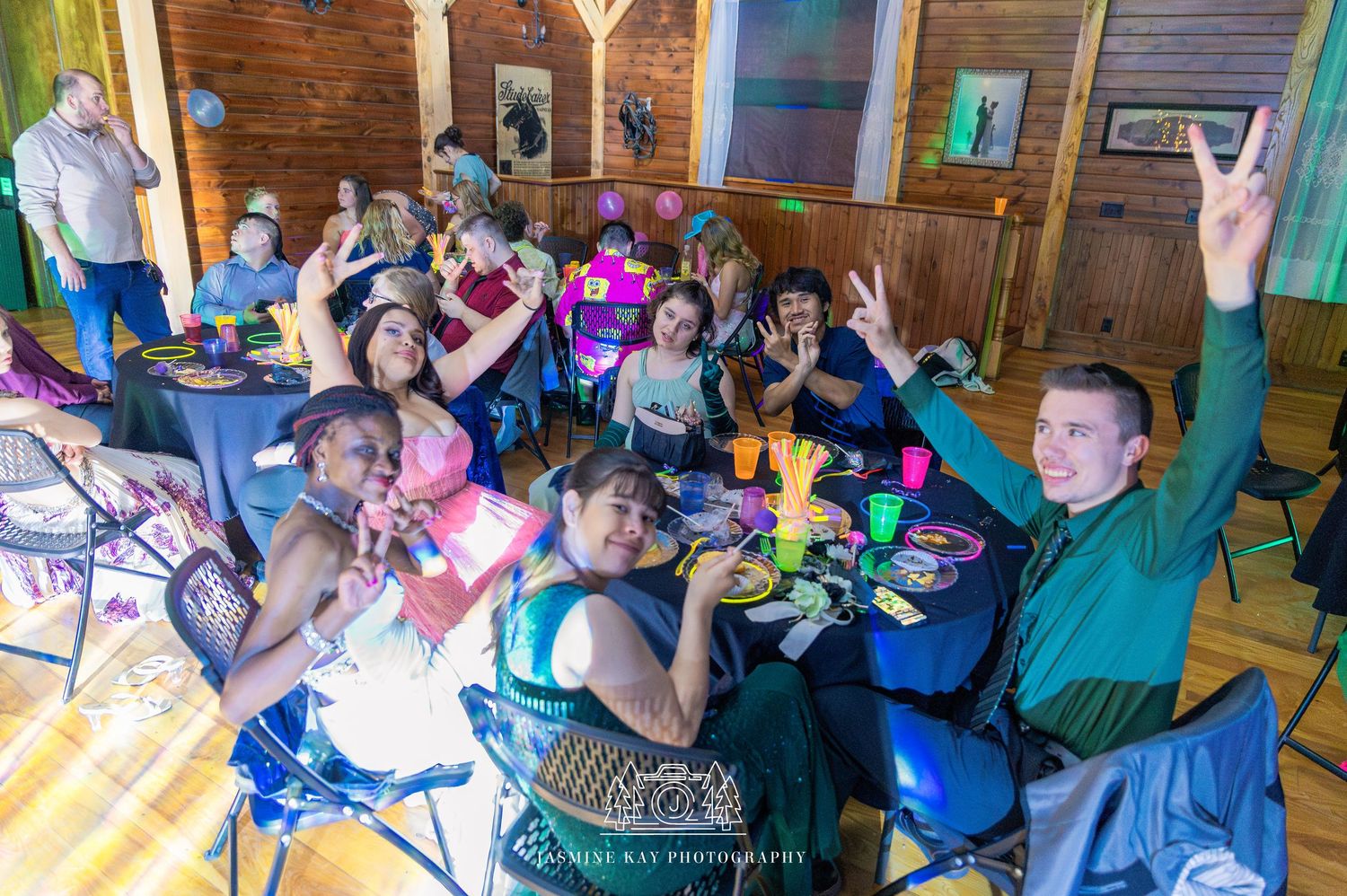 A group of excited people cheer and raise their arms while watching an event in a rustic wooden room.