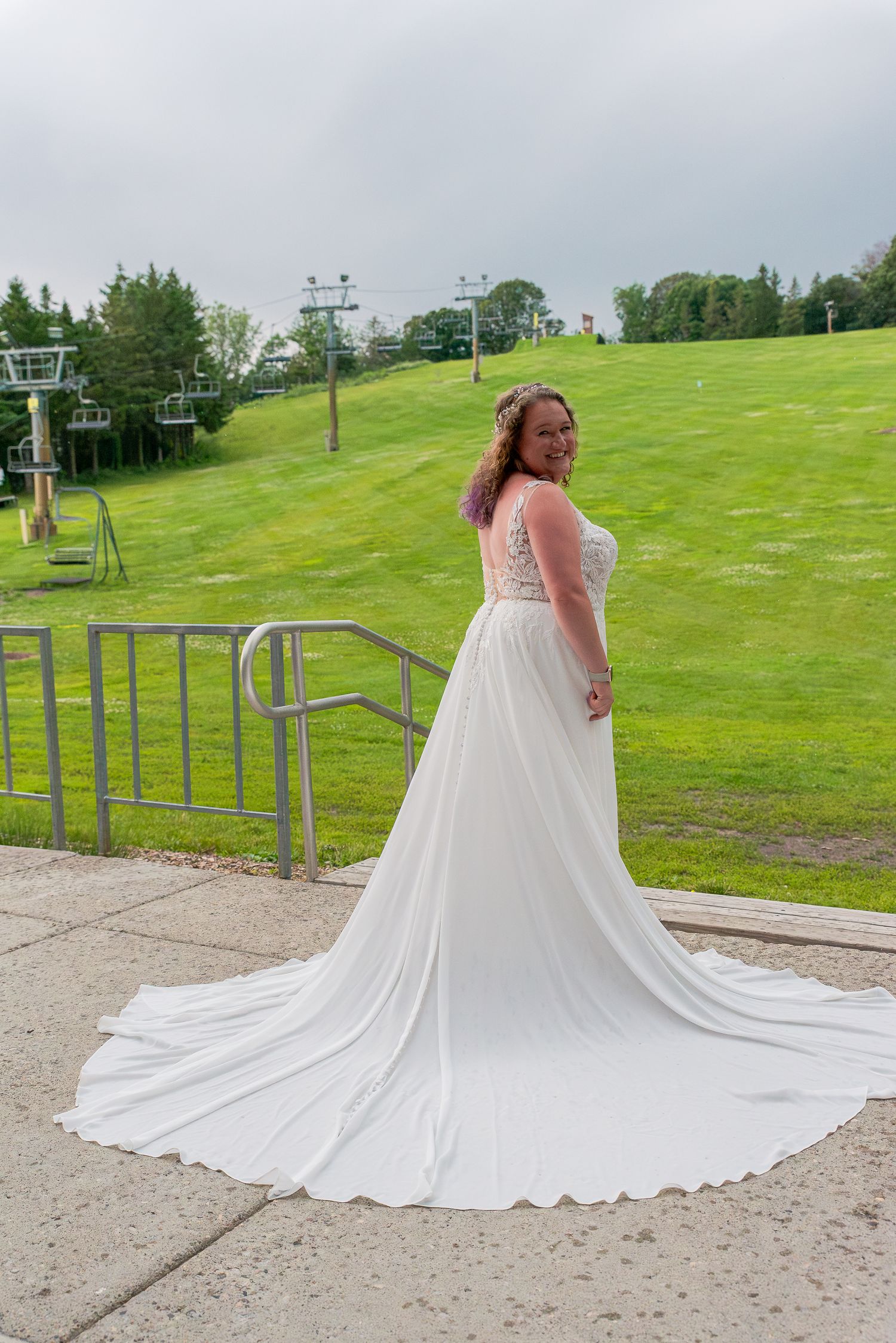 A flowing white wedding dress with a dramatic cathedral-length train displayed on a grassy hillside with ski lifts.