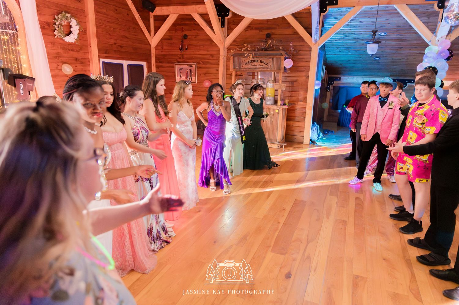 Wedding guests dancing together on a wooden dance floor in a rustic barn venue with warm lighting.