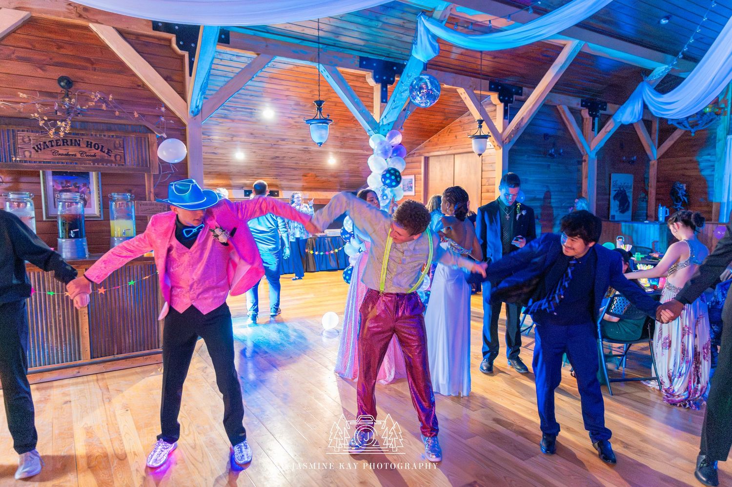 People dancing and enjoying themselves in a large wooden ballroom with colorful blue and pink lighting effects.
