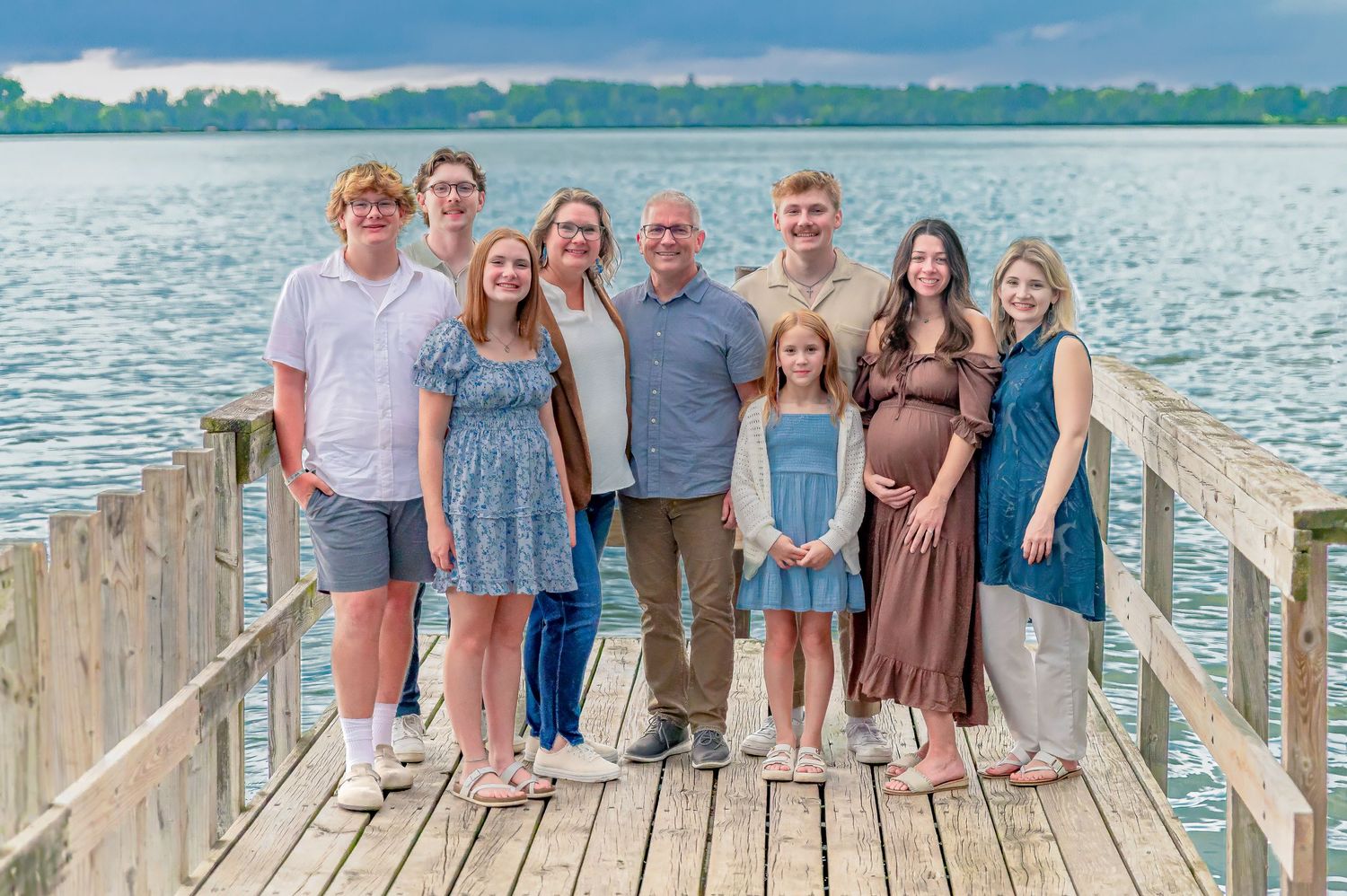 A group of people pose together on a wooden dock by a lake on a sunny summer day.