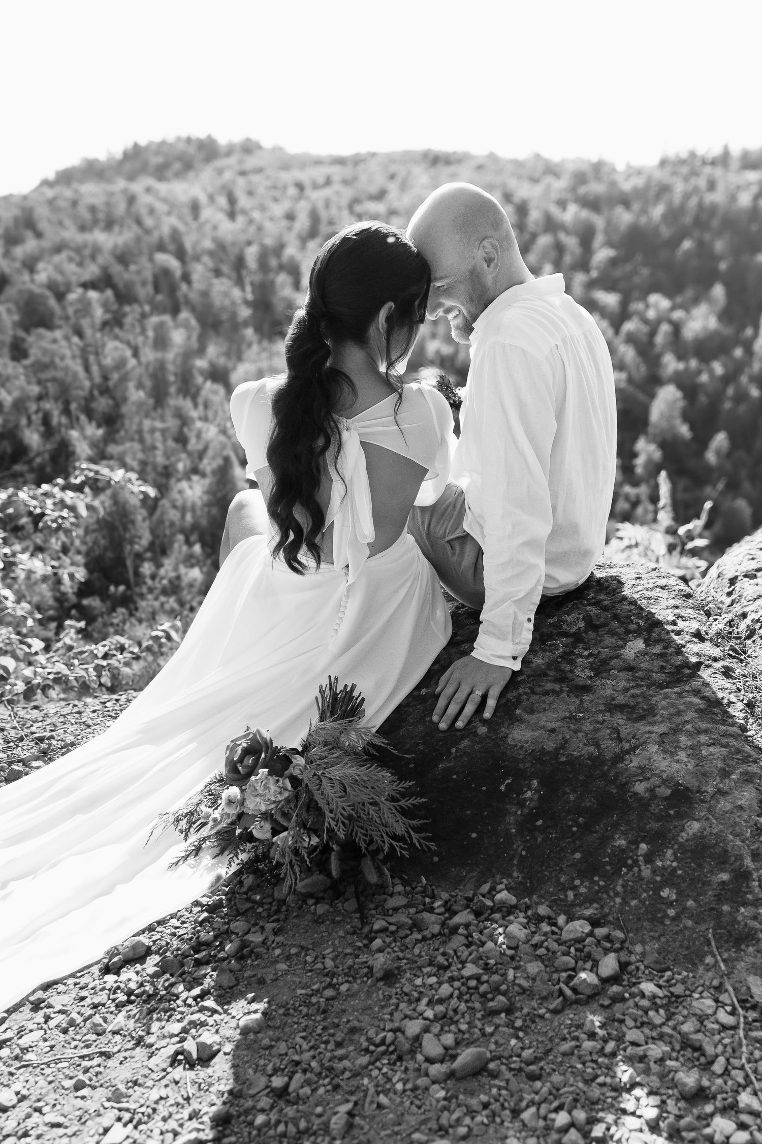 A black and white wedding portrait capturing an intimate moment between newlyweds on a hilltop.