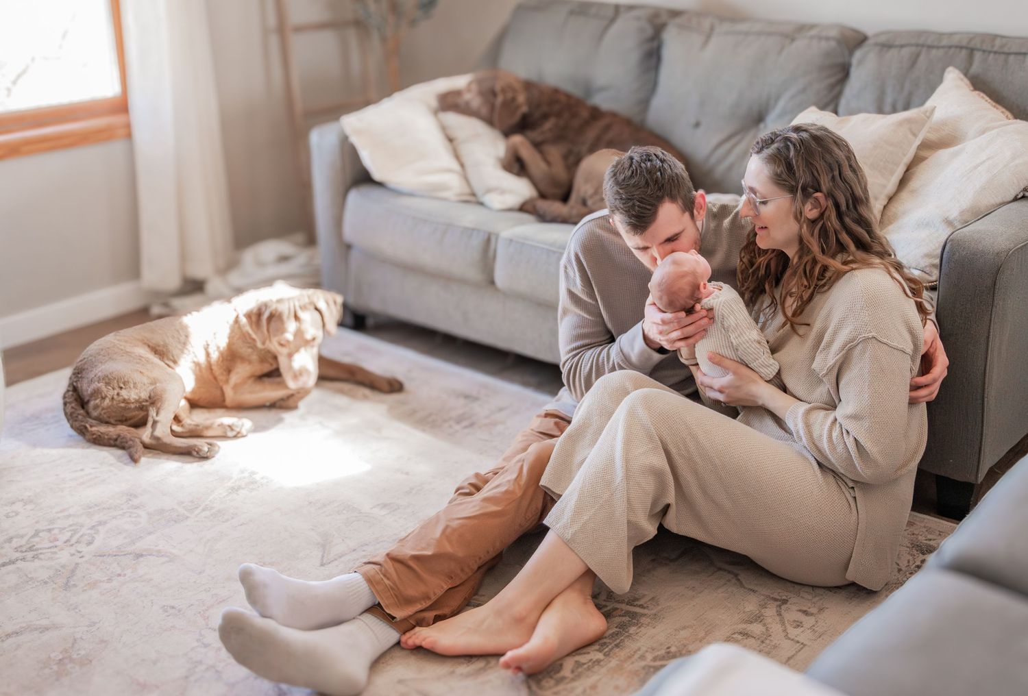 A couple relaxes together on a cozy gray couch with their pet cat in a bright, modern living room.