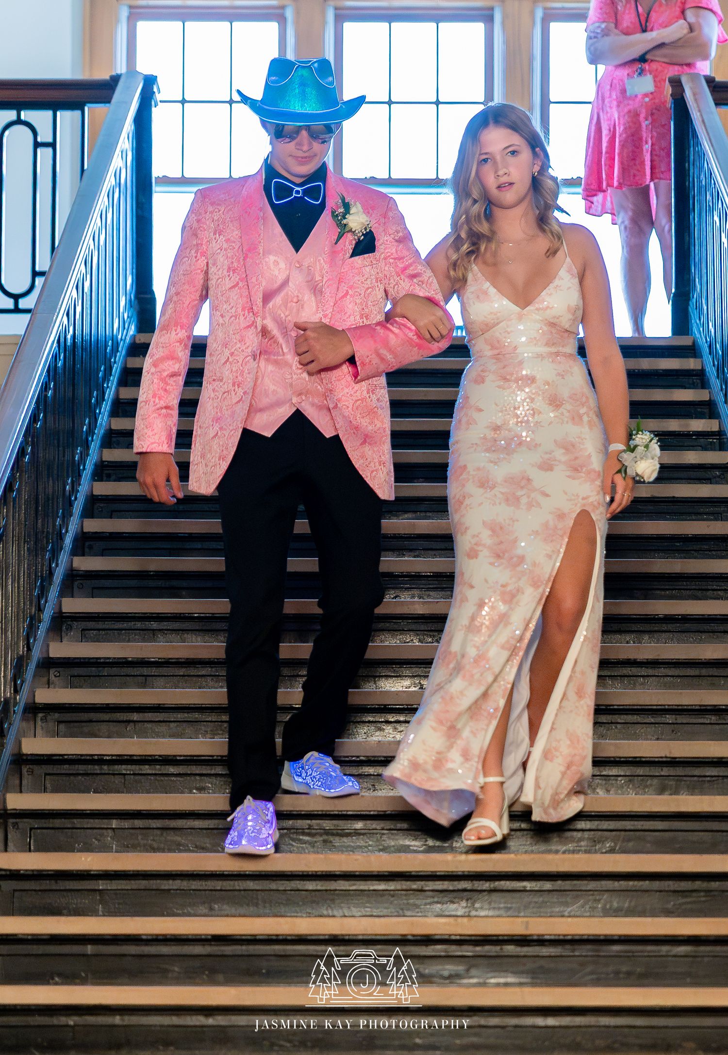 Wedding couple sits casually on rustic wooden stairs wearing pink and white attire with blue sneakers.