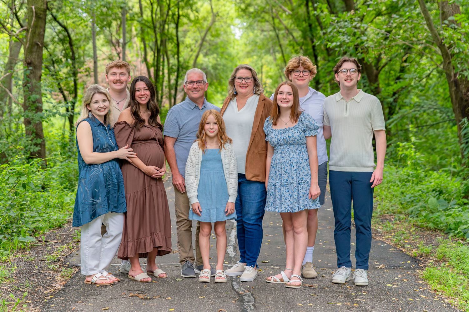 A group of people stand together on a wooded path wearing casual spring attire in natural lighting.