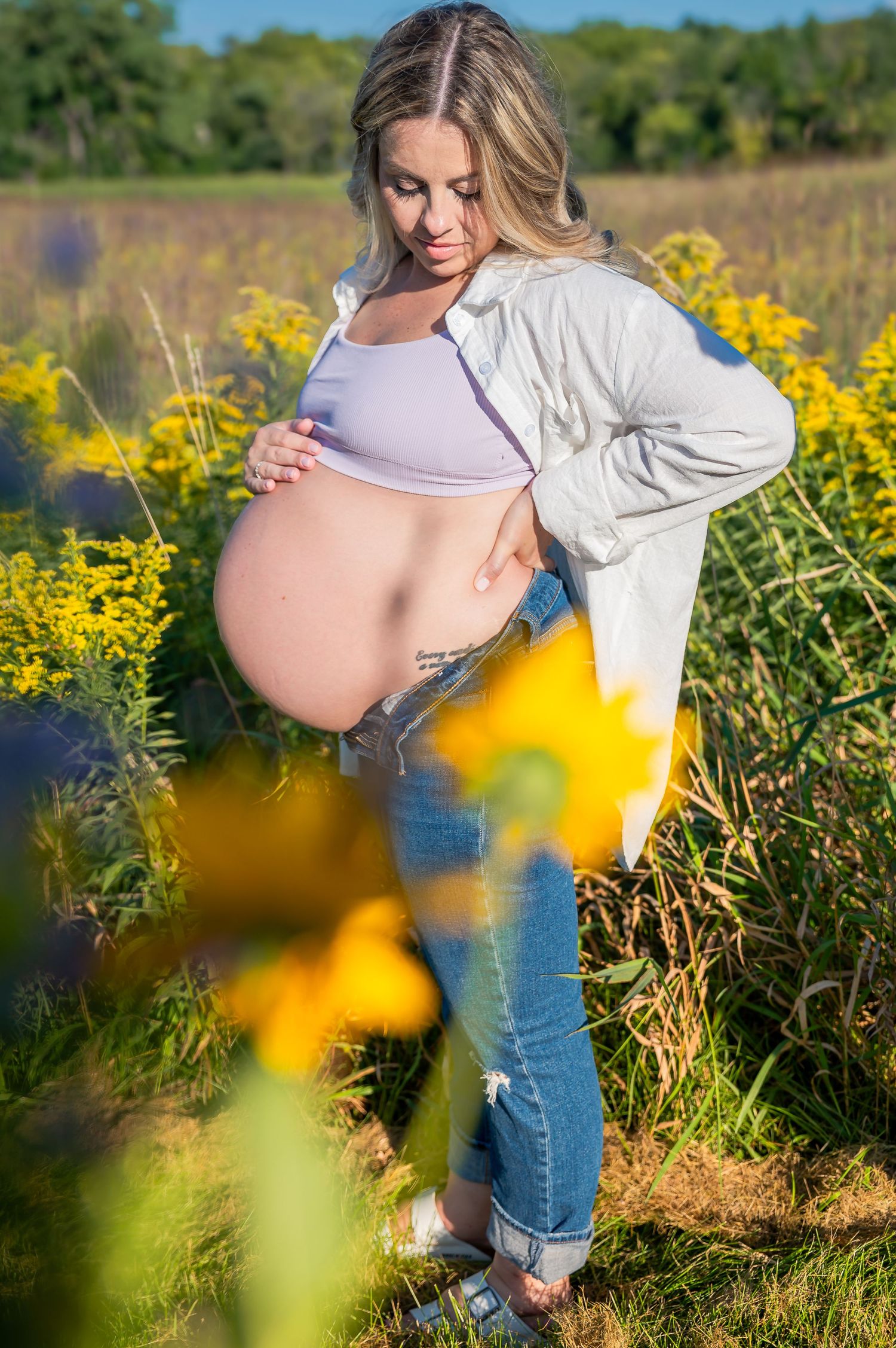 A maternity photoshoot in a field of bright yellow wildflowers on a sunny summer day.