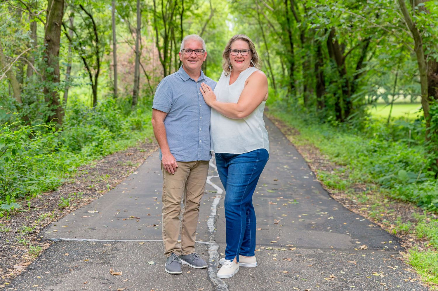 A couple walks together on a tree-lined path in a lush green park during summer.