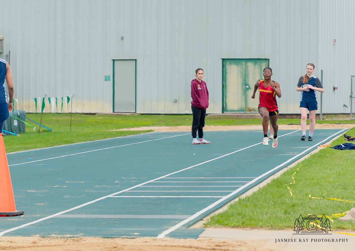 Athletes compete in long jump events on an indoor track and field facility with multiple parallel runways.