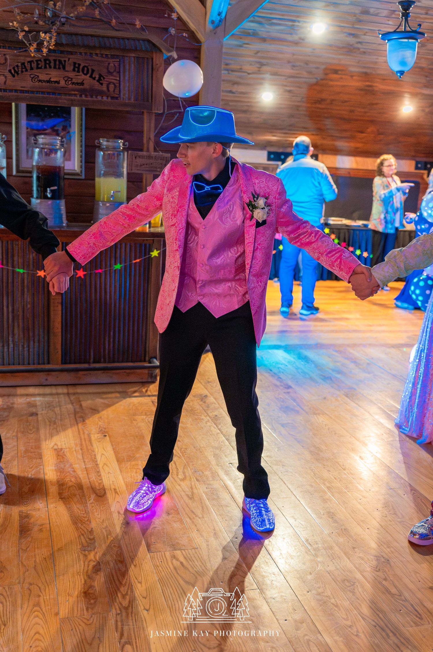 Dancer in pink vest and black pants performs a line dance sequence on wooden dance floor with blue lighting.