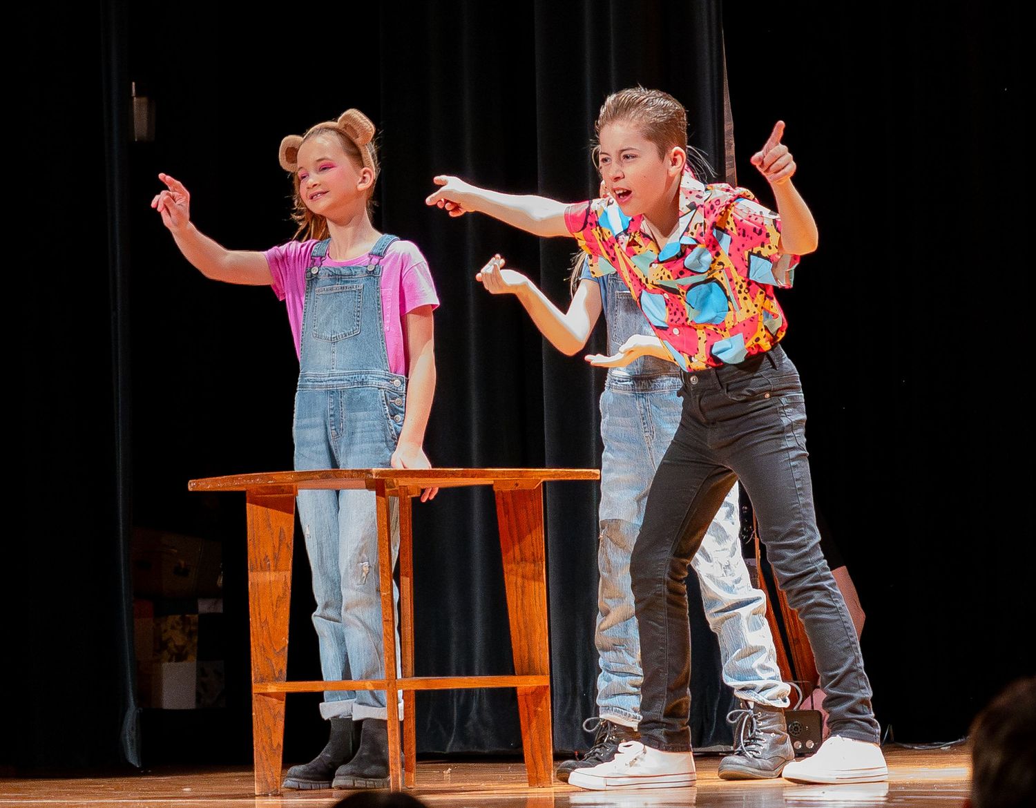 Stage performers interact with wooden furniture during a dramatic scene in a theatrical production.