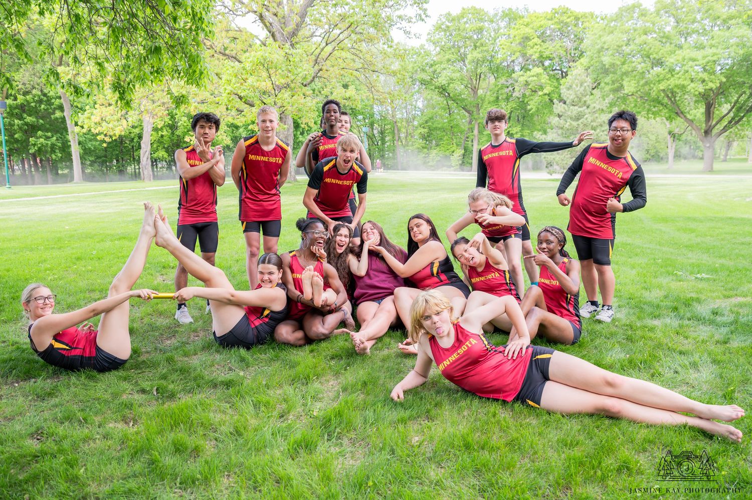 Soccer team members in red jerseys lay on grass in a playful formation during an outdoor photo session.