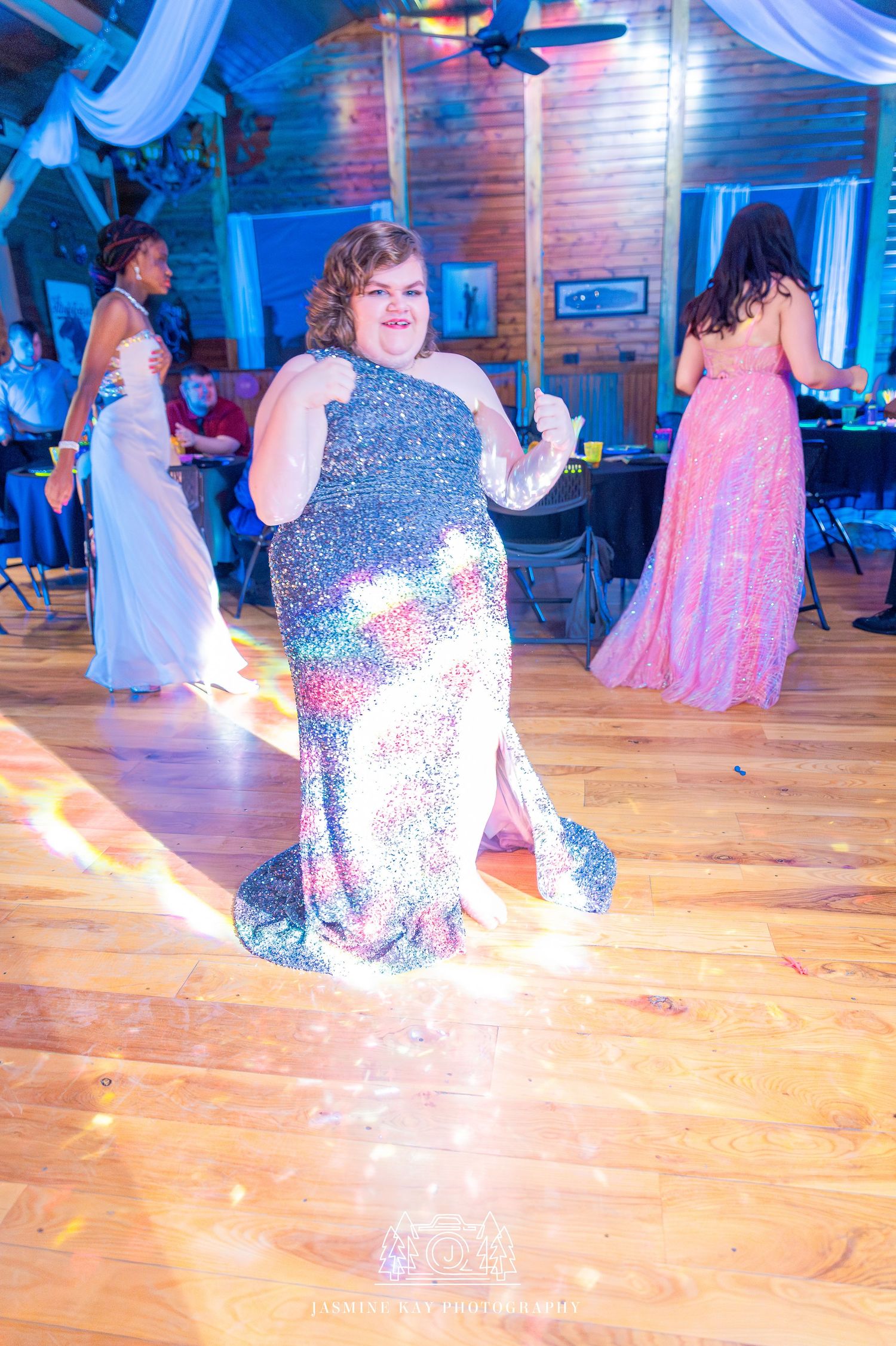 Dancers in formal attire perform on a polished wooden dance floor under blue lighting at an indoor venue.