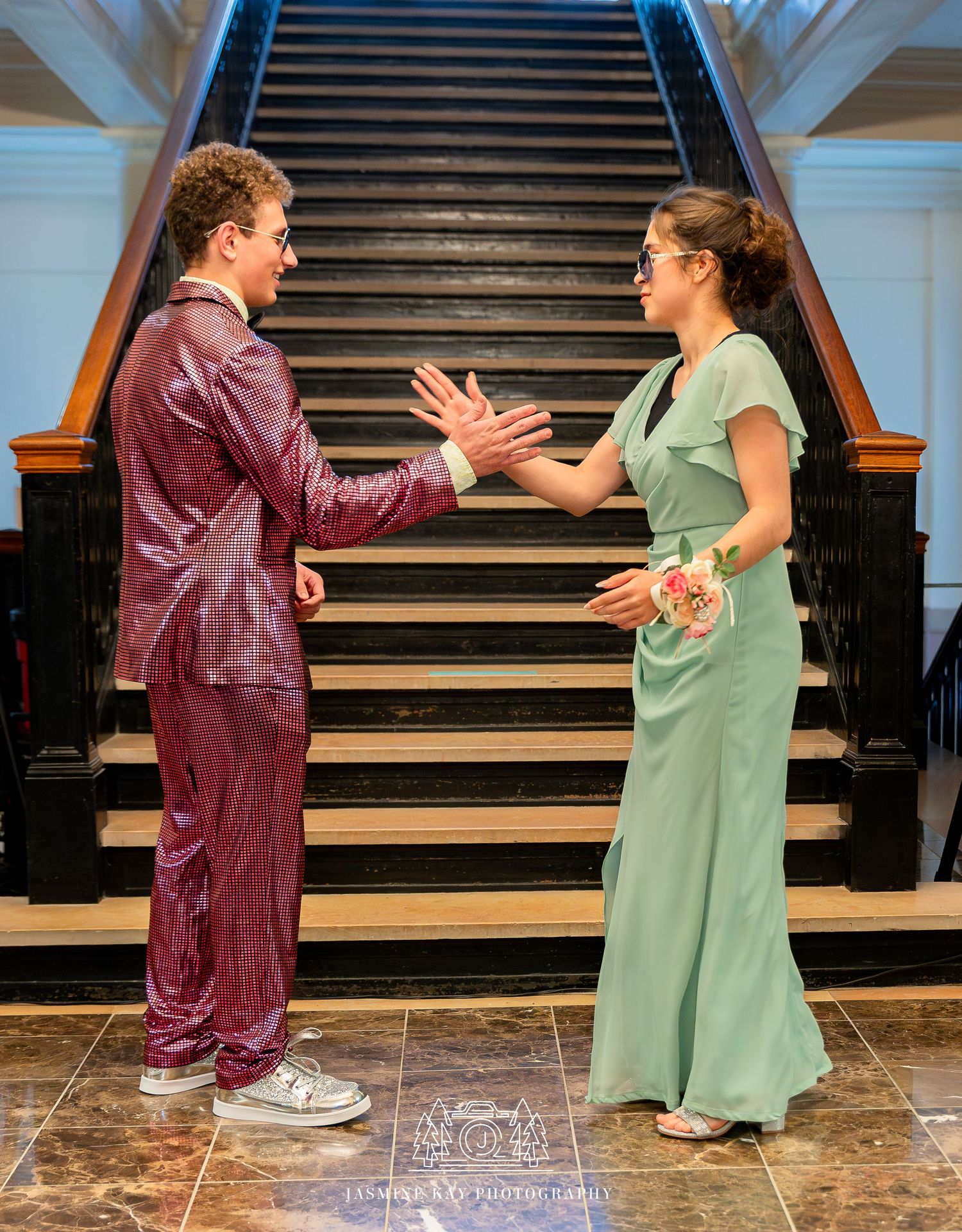 Two people in casual attire engage in an animated conversation near a staircase in an indoor setting.