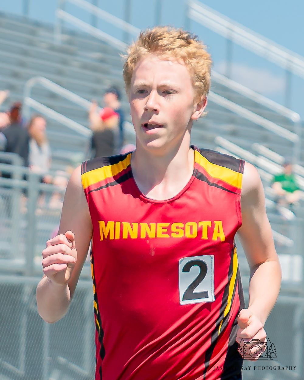 Track athlete in Minnesota uniform sprinting during competitive race on sunny day.