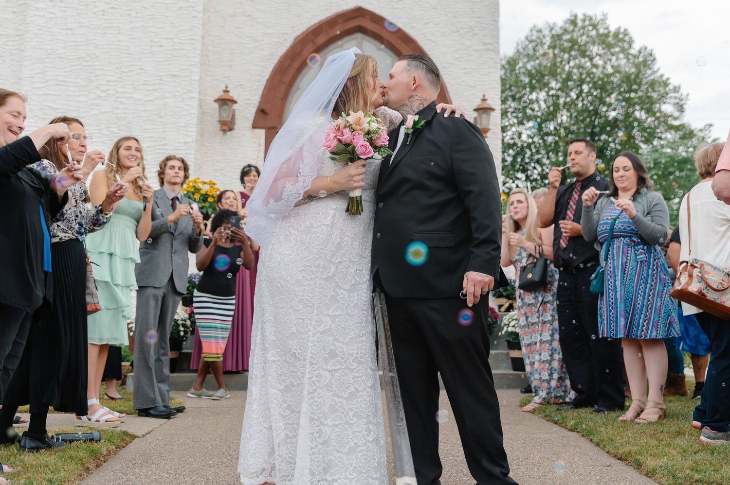 Wedding guests celebrate as newlyweds share their first kiss outside a church entrance.