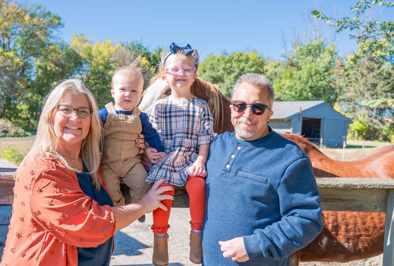 A family enjoys a sunny autumn day together at a rustic barn or farm setting.