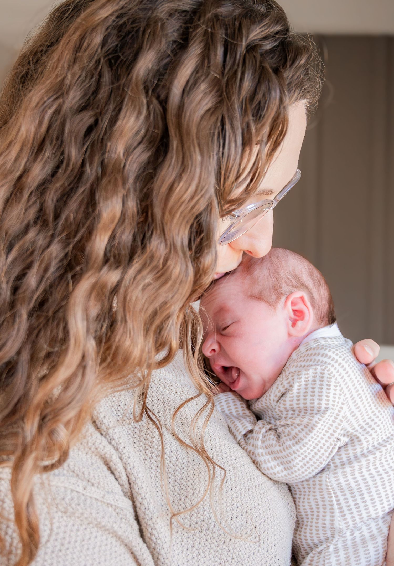 A tender moment between parent and newborn baby in soft natural light wearing cozy cream sweaters.