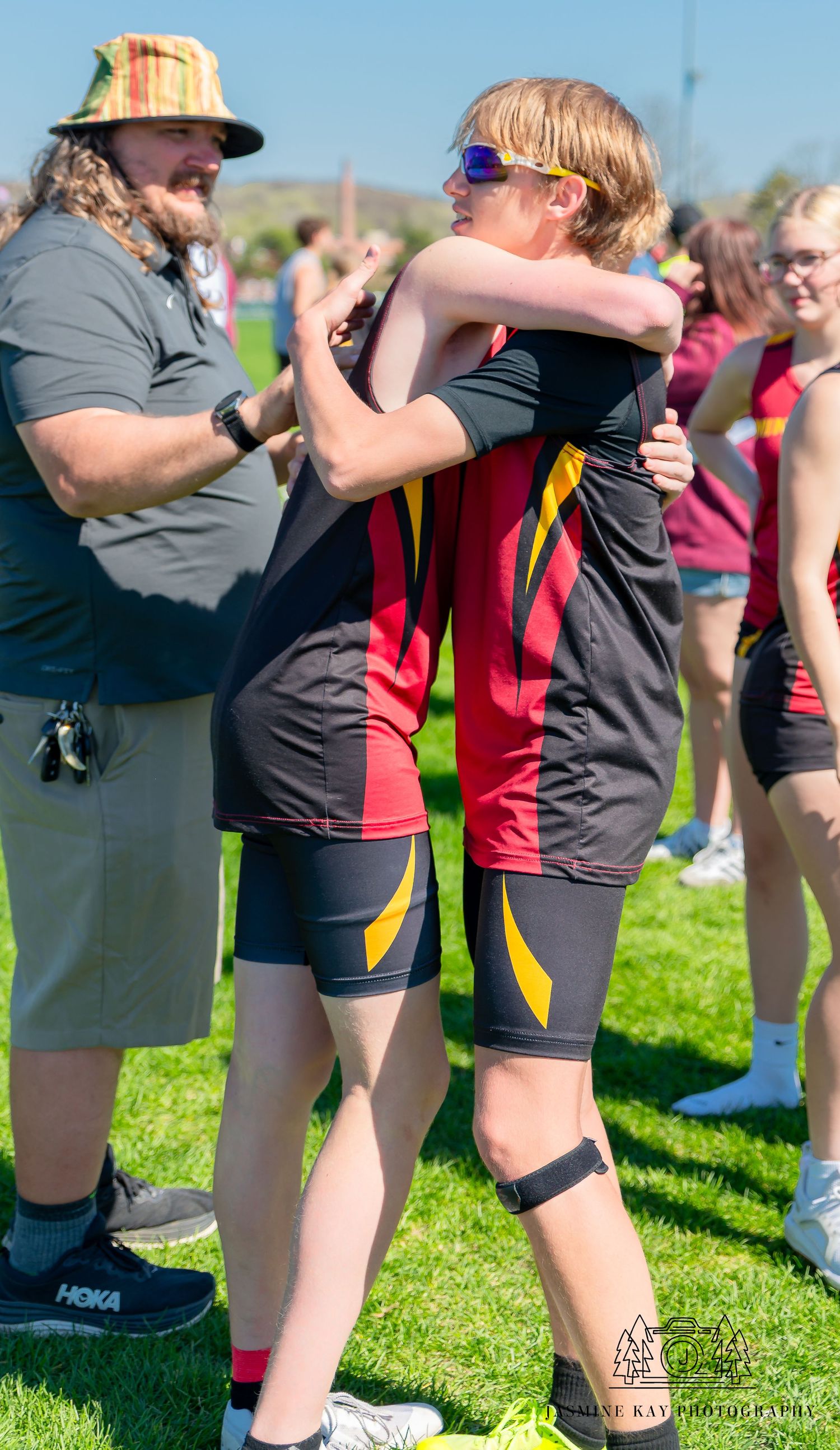 Athletes in black and red uniforms stretching together on a sunny grass field during training.