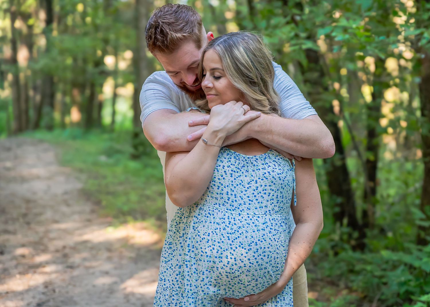 A couple embraces tenderly on a sunlit forest path during a romantic outdoor photoshoot.