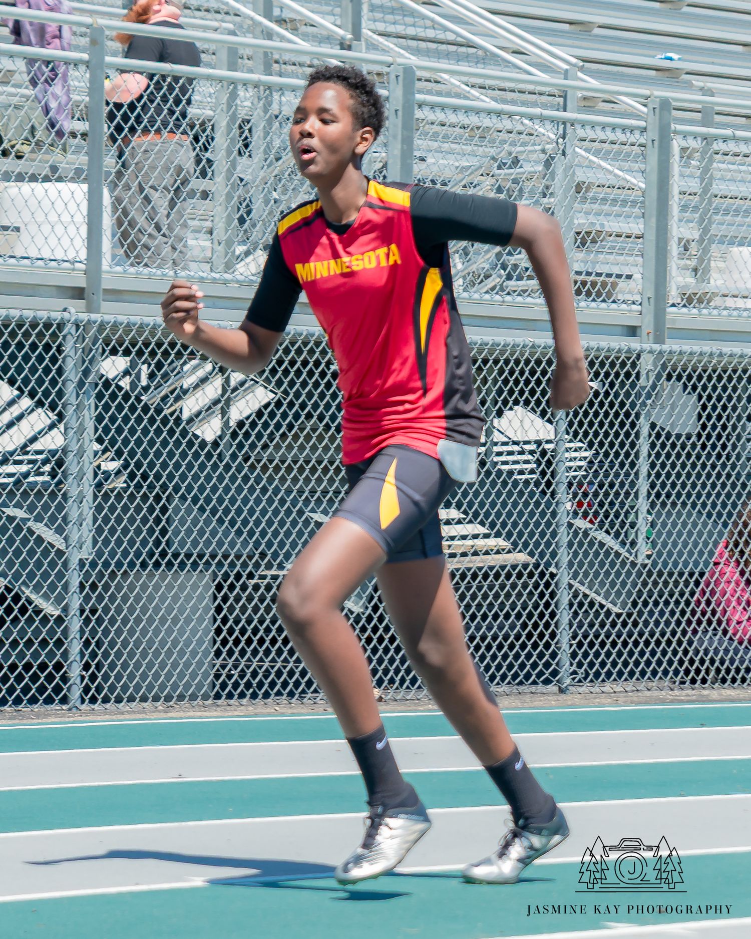 Athlete in red and yellow uniform sprinting on outdoor running track during competition.