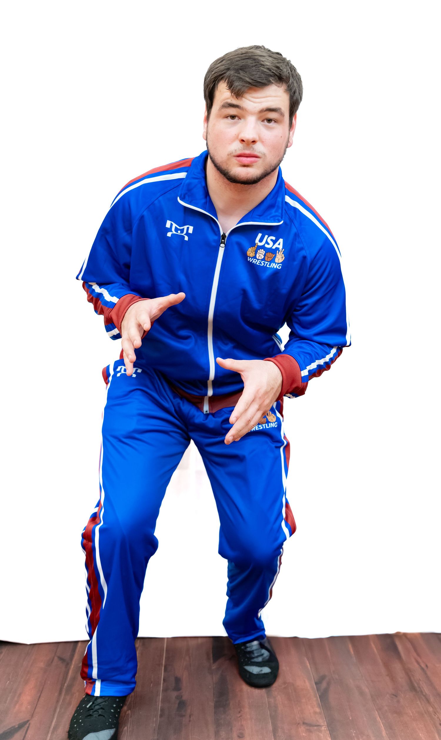 Person in blue USA wrestling team uniform stands in athletic stance on wooden flooring.