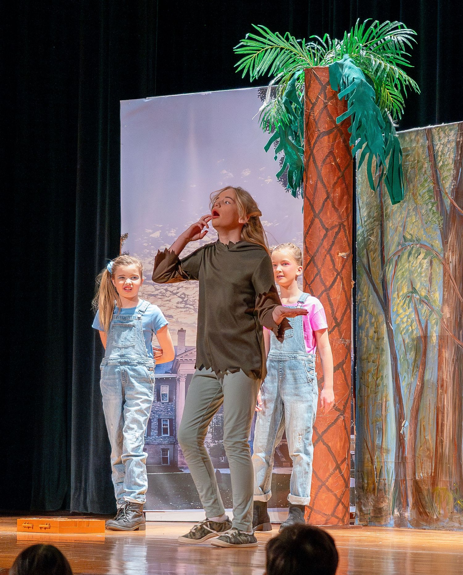 Stage performers in casual attire dancing against a woodland theatrical backdrop.