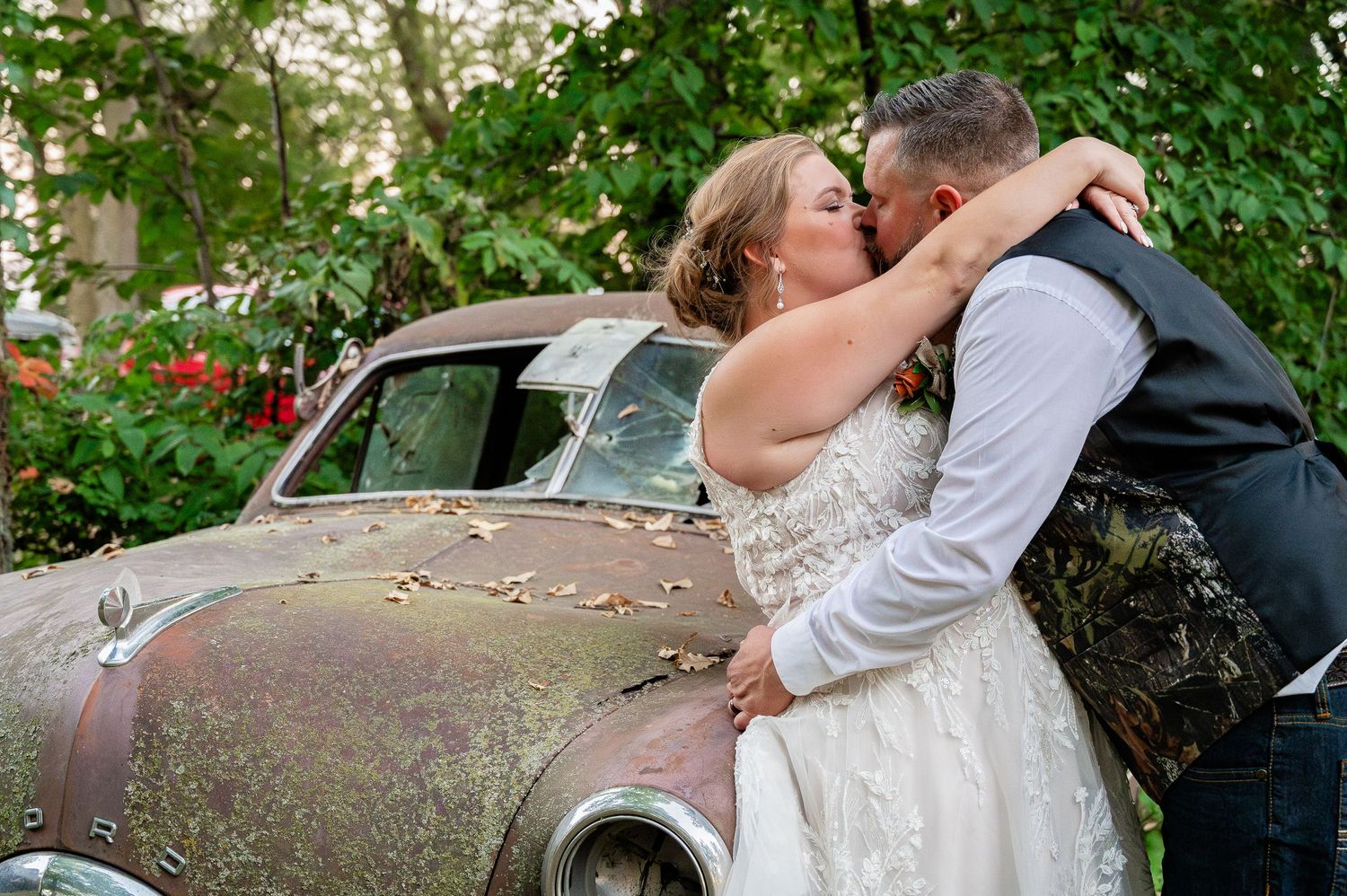 Romantic moment shared against vintage car backdrop surrounded by greenery.