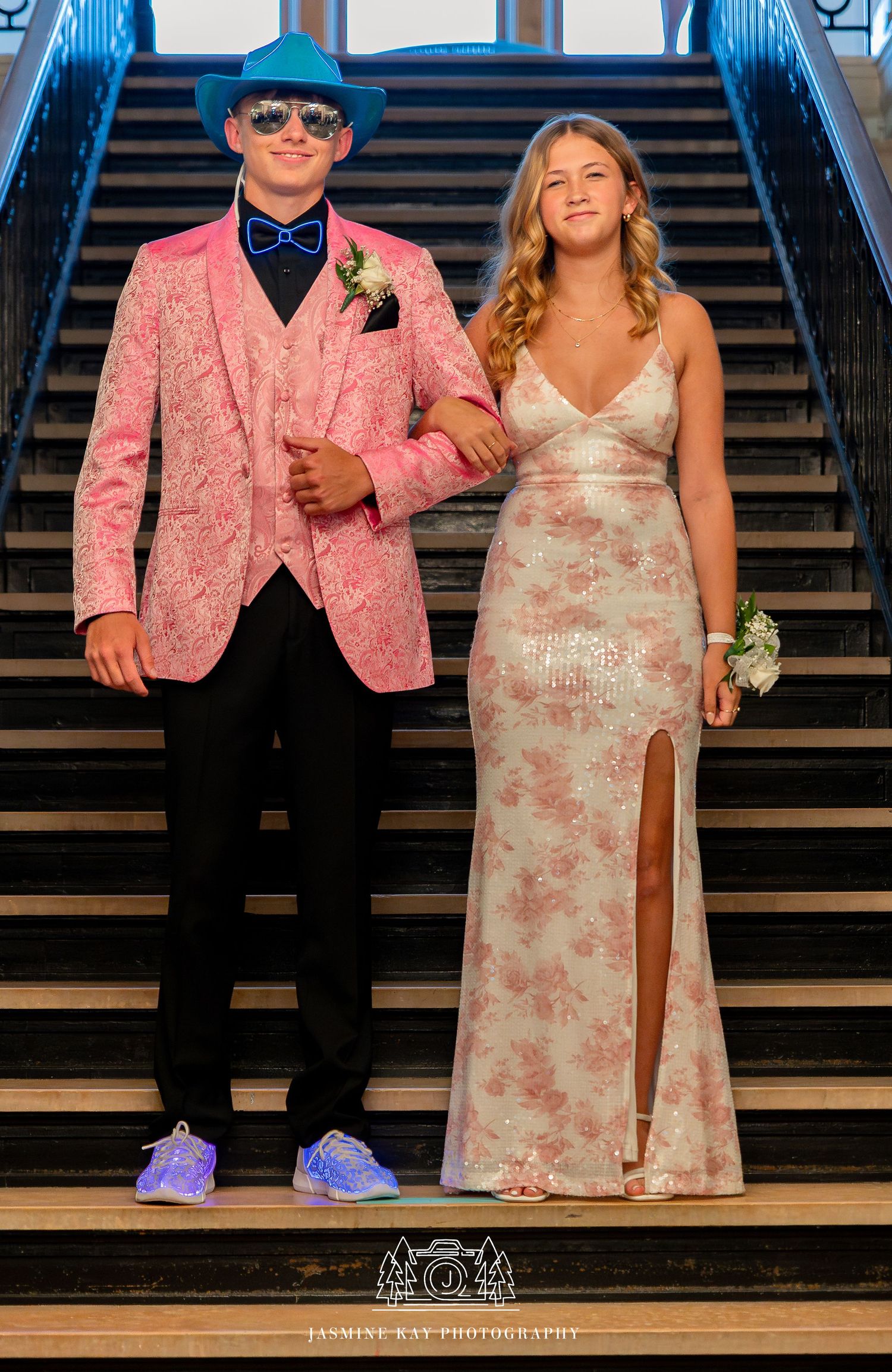 A couple stands on wooden stairs, with the person on the right wearing a floral dress and the left in a pink jacket.