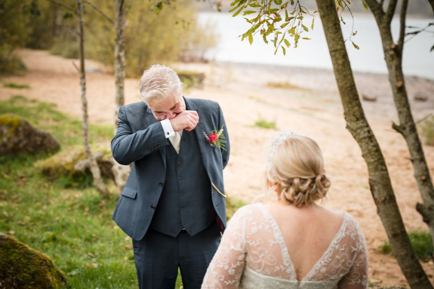 A tender wedding moment captured between newlyweds on a lakeside path surrounded by autumn birch trees.
